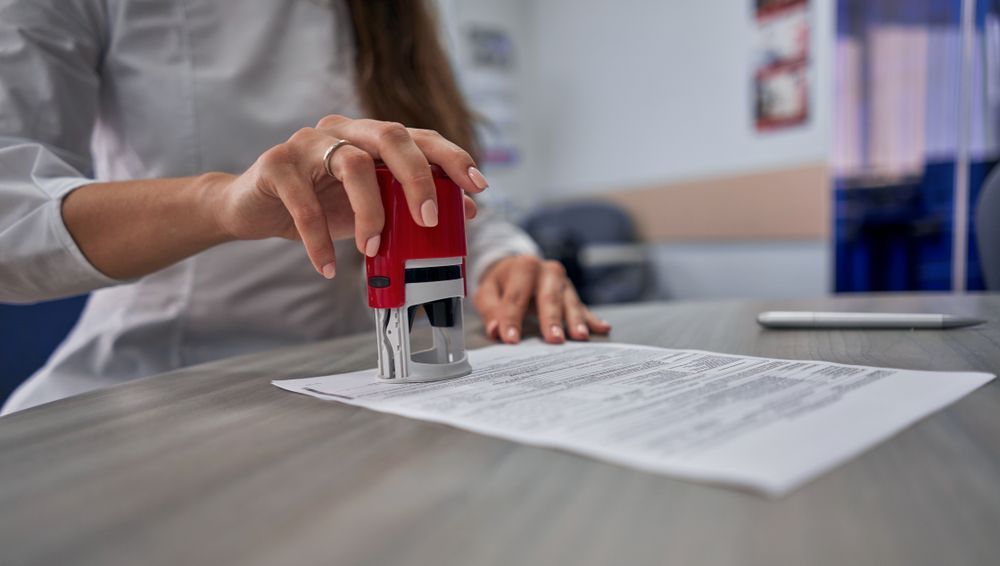 A woman is putting a stamp on a piece of paper.