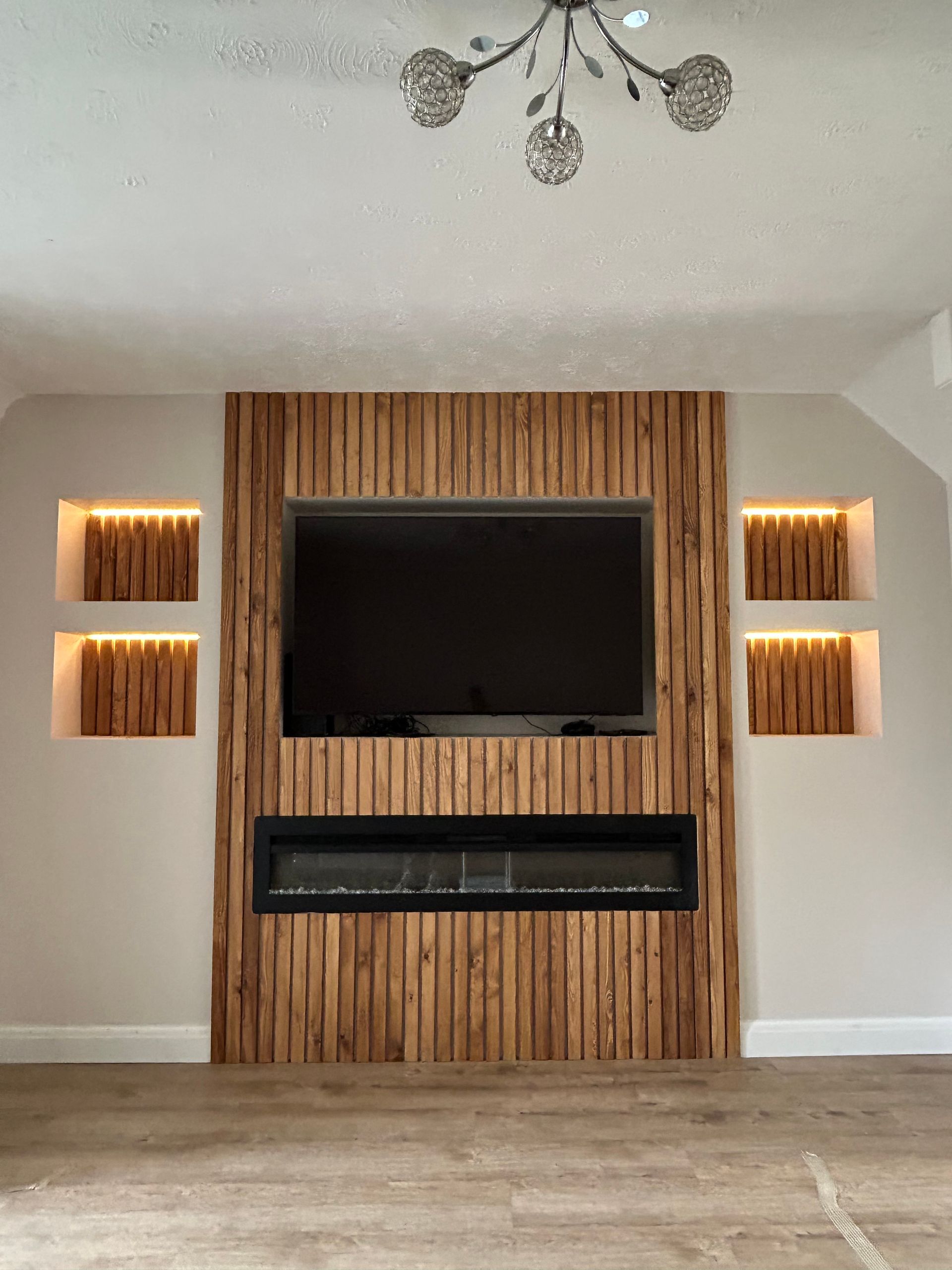 Living room wall with mounted TV, electric fireplace, and vertical wood paneling with lit shelves