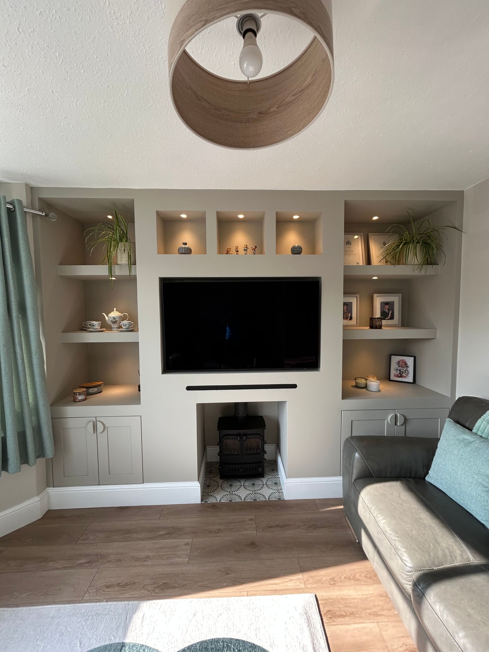 Living room with a wall-mounted TV, built-in shelves, fireplace, and gray sofa in warm neutral tones