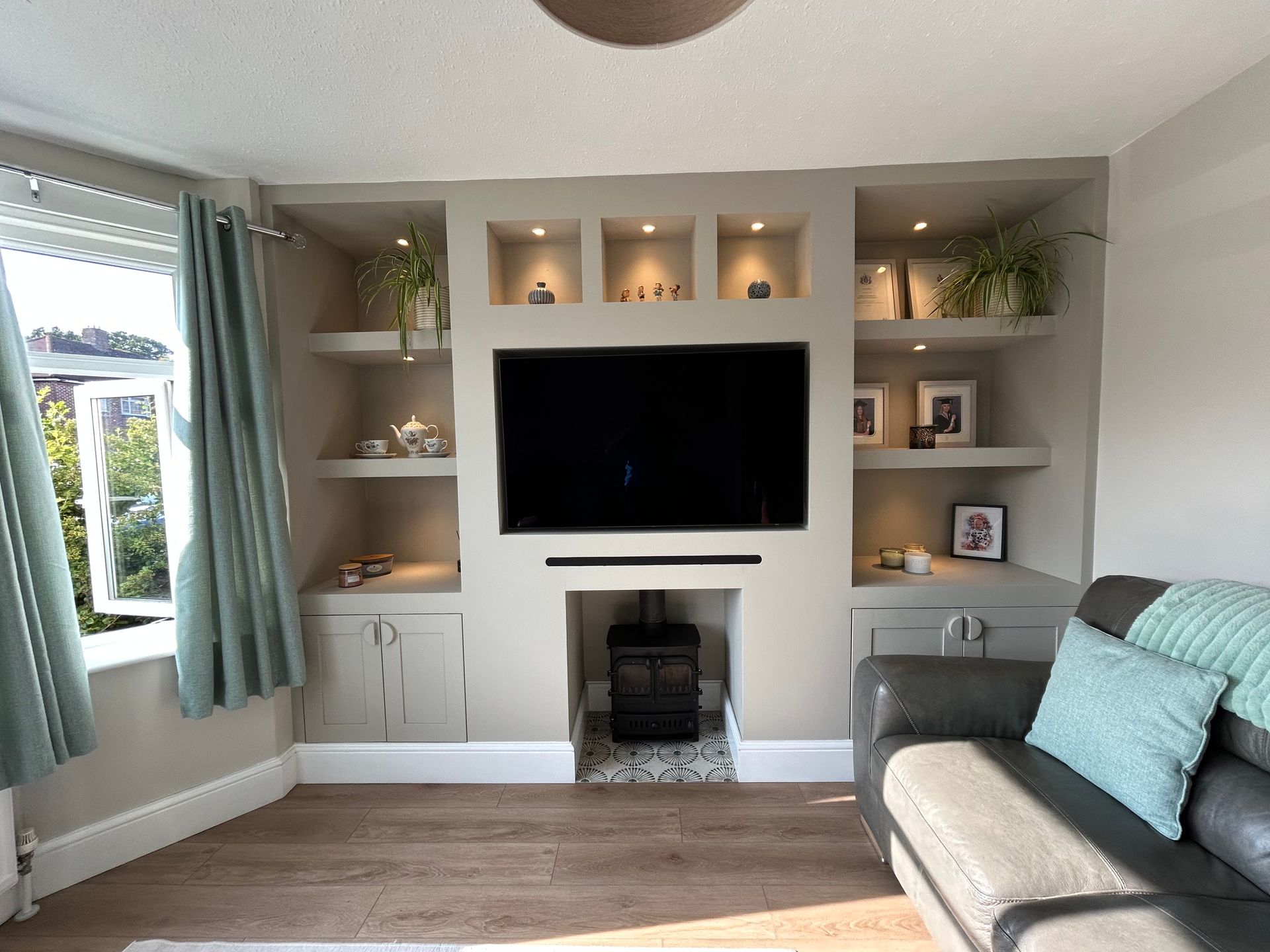 Living room with wall-mounted TV, built-in shelves, fireplace, and a gray sofa with teal cushions.