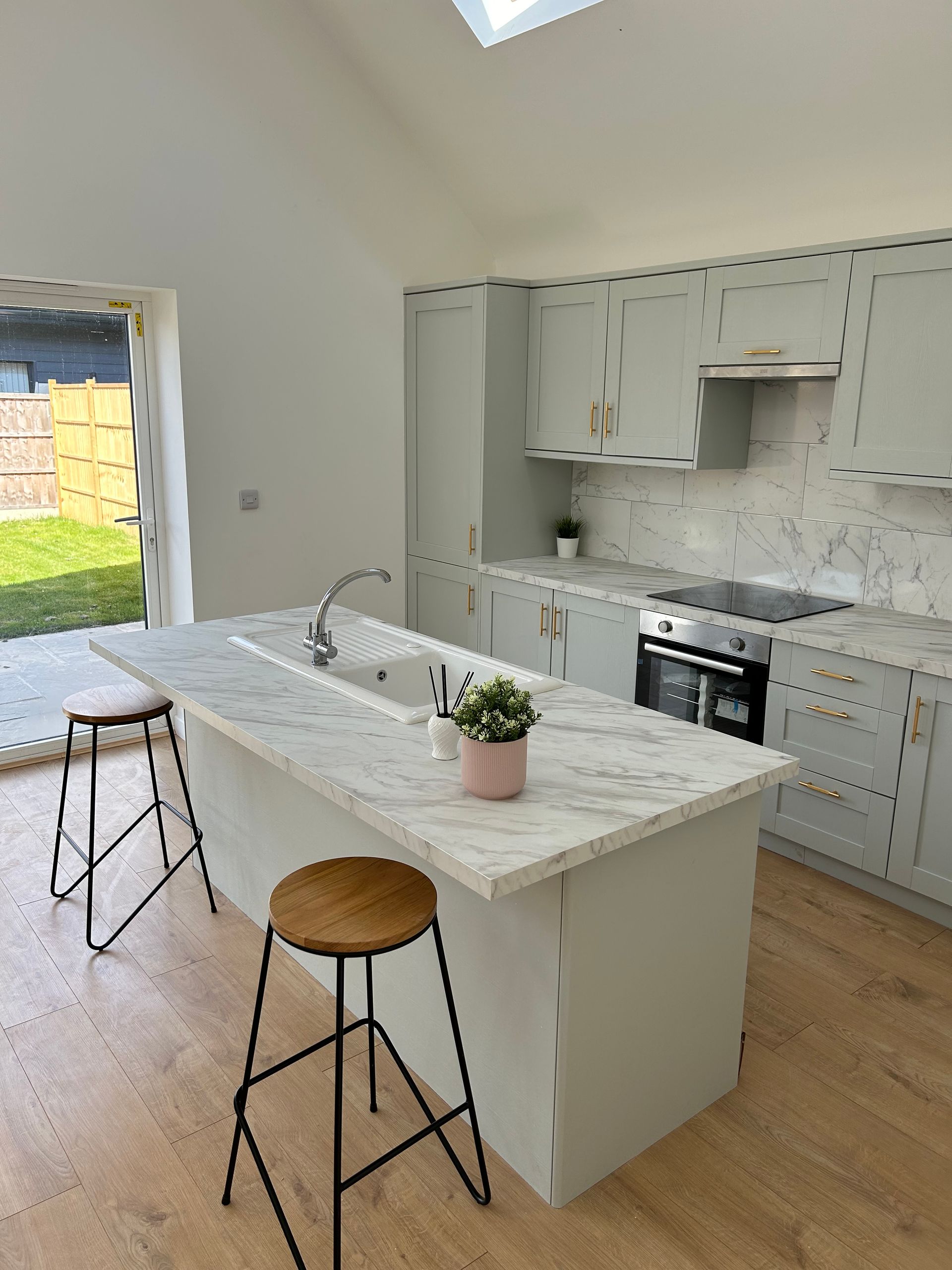 Bright modern kitchen with white cabinets, marble island, and stools near a glass door to the yard
