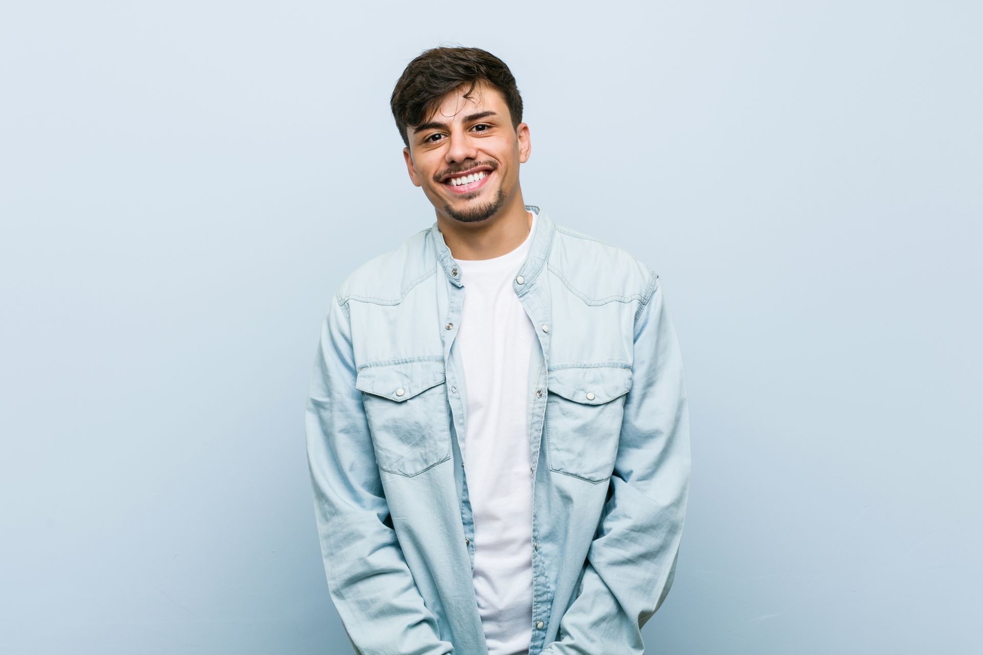 A young man is standing in front of a blue wall and smiling.