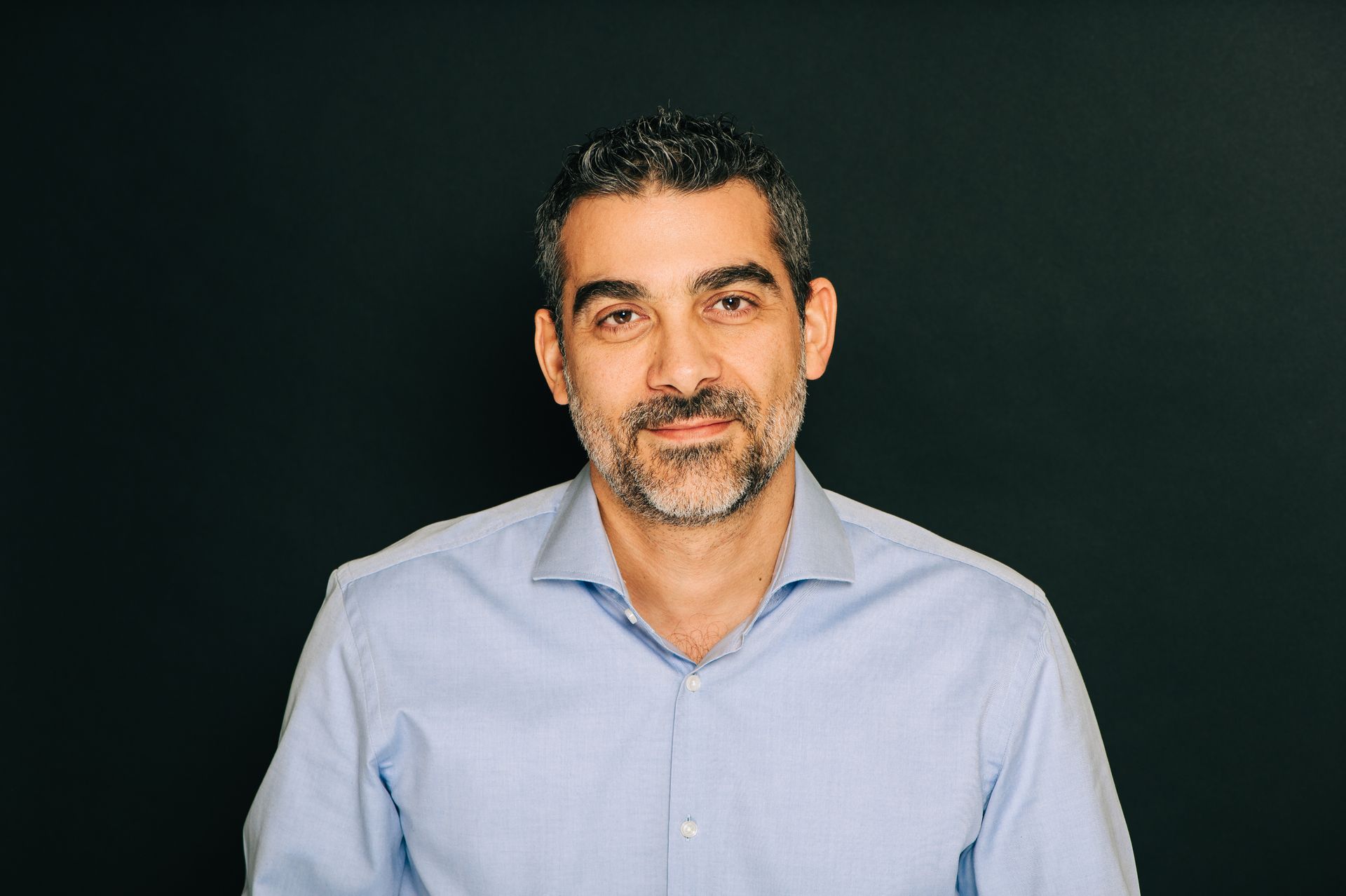 A man with a beard is wearing a blue shirt and smiling for the camera.