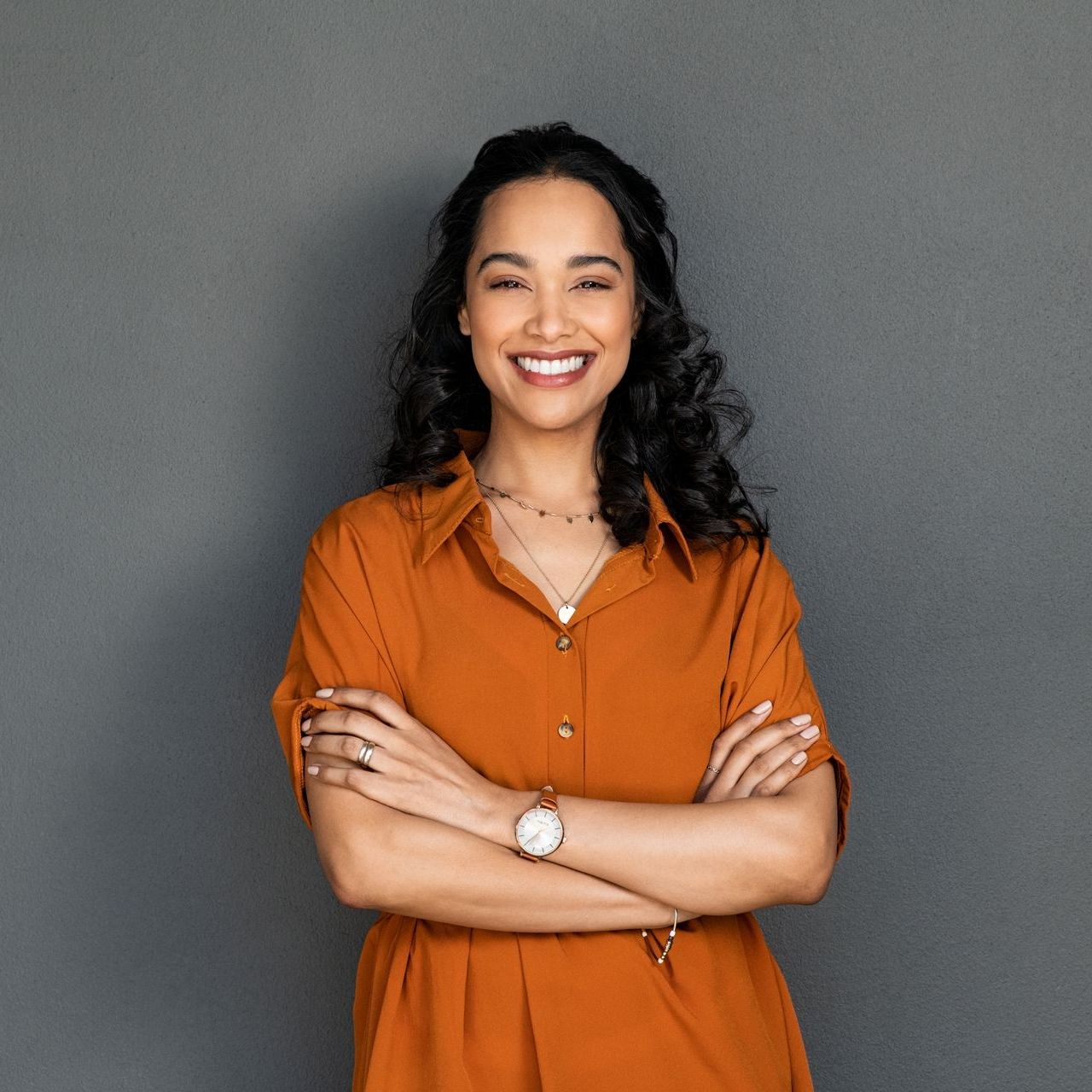 A woman in an orange dress is smiling with her arms crossed.