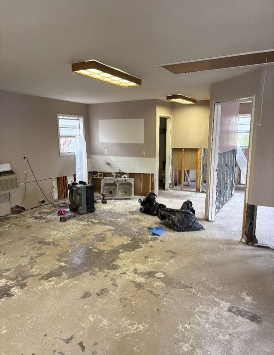 A room undergoing renovation with exposed walls, debris on the floor, and overhead lighting.
