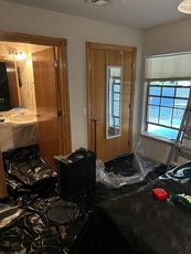 Room with doors, window, and covered furniture during renovation; plastic sheeting on floor.