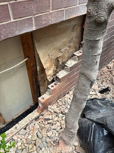 Damaged brick wall with exposed interior, next to a tree and gravel.