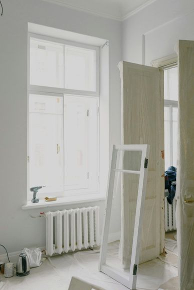 White room with window and radiator, a disassembled door frame, and another door.