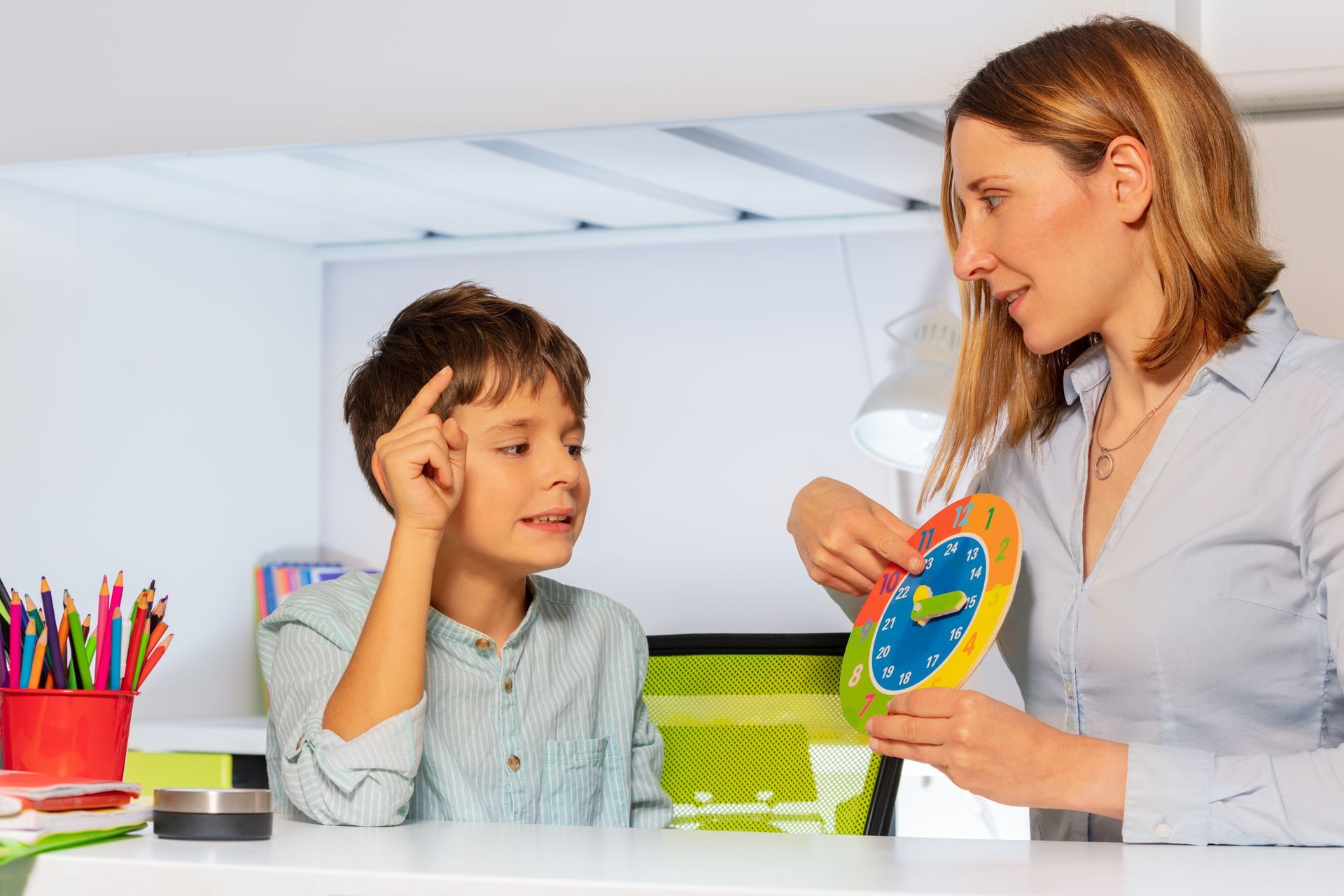 Woman teaching boy about time using a clock, indoors.