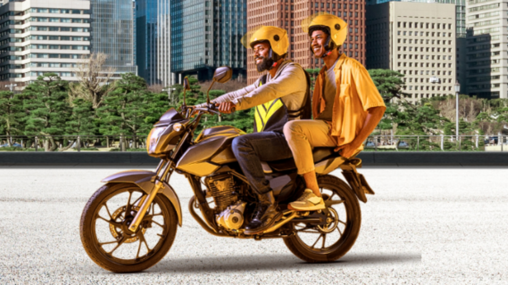 Dois homens em uma motocicleta dourada com capacetes amarelos, em frente a prédios. Um deles veste um colete refletor.