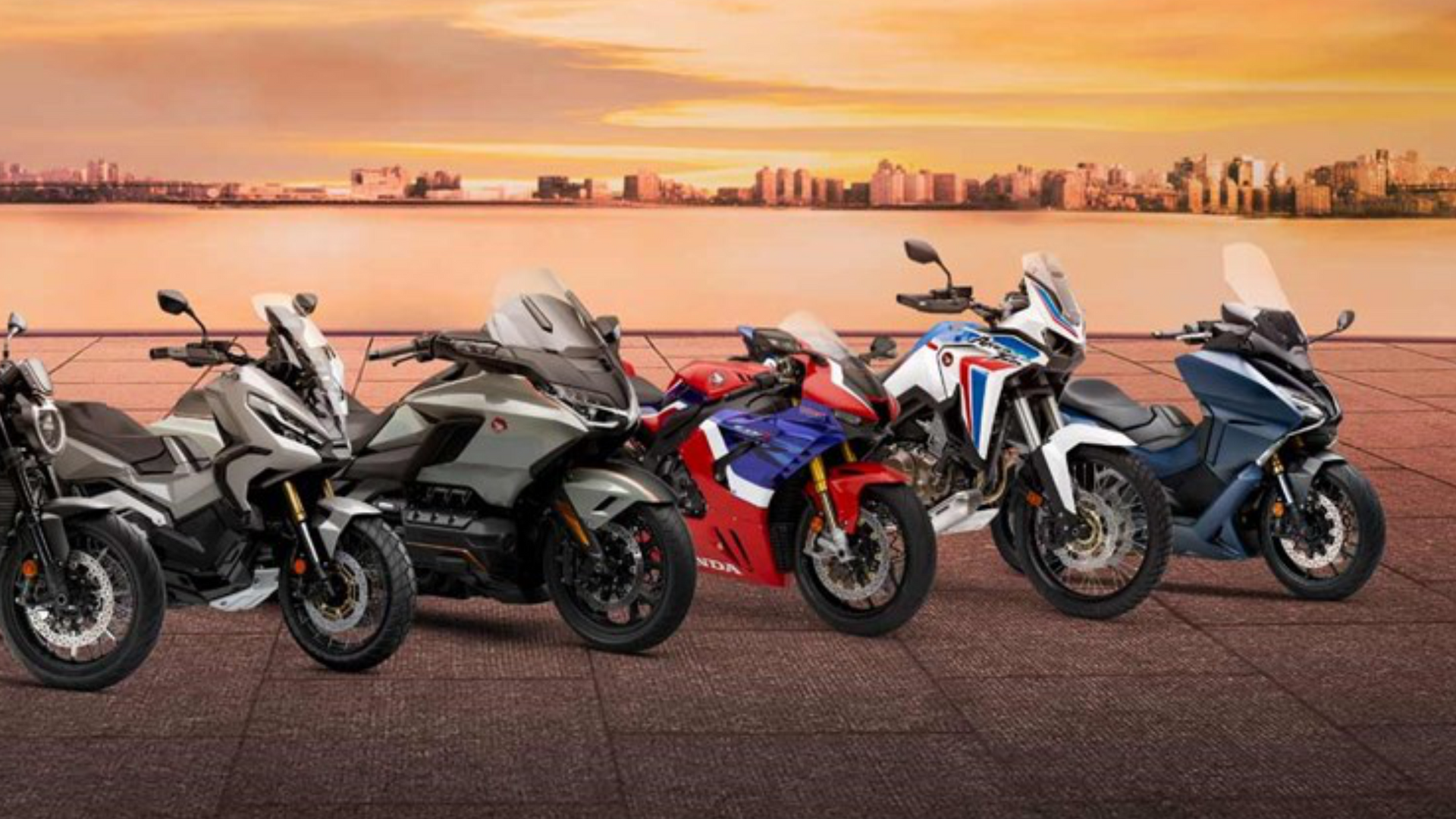 Cinco motocicletas Honda estacionadas em fila, com a paisagem urbana ao fundo ao pôr do sol.