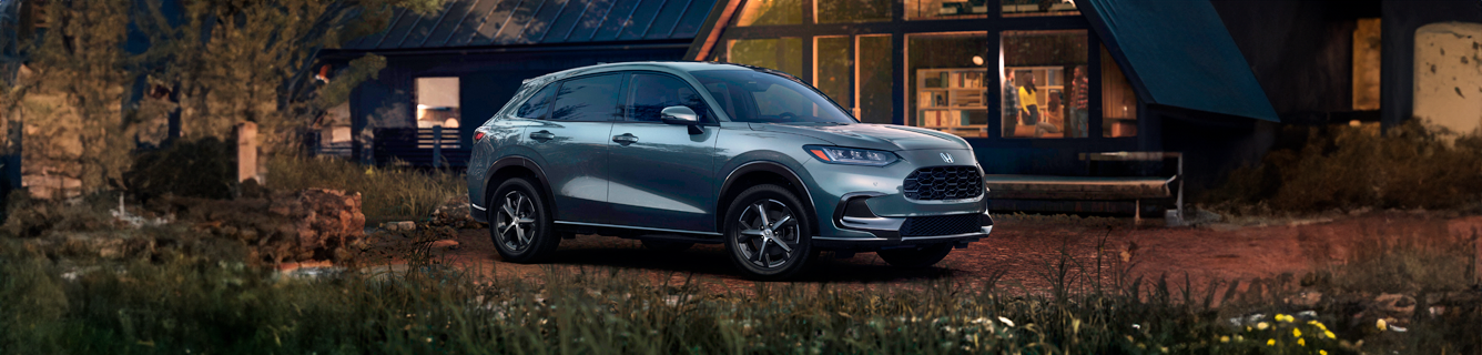 Um SUV prateado estacionado em frente a uma casa ao entardecer.