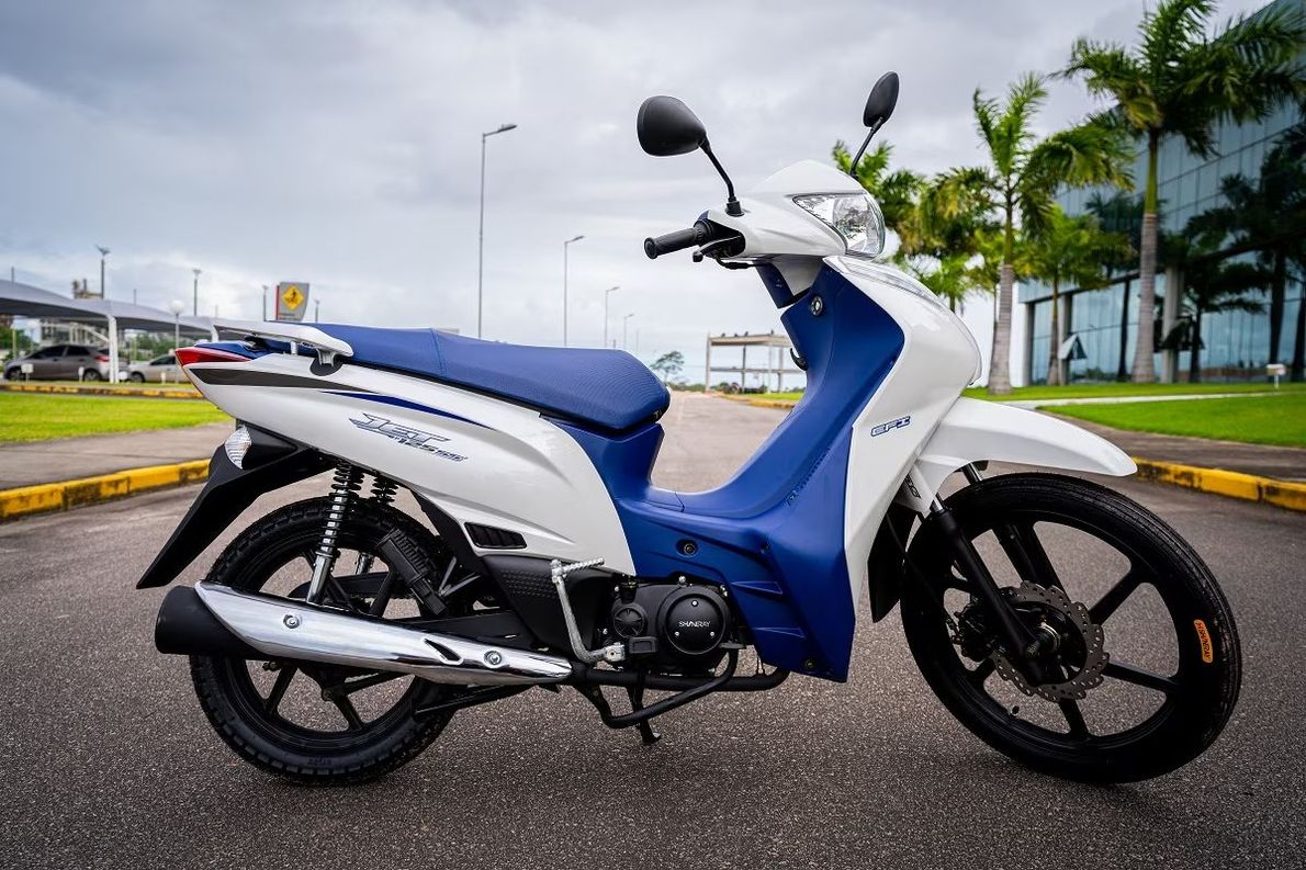 Motocicleta vermelha e prateada estacionada em uma rua da cidade; possui pneus para fora de estrada e motor preto.
