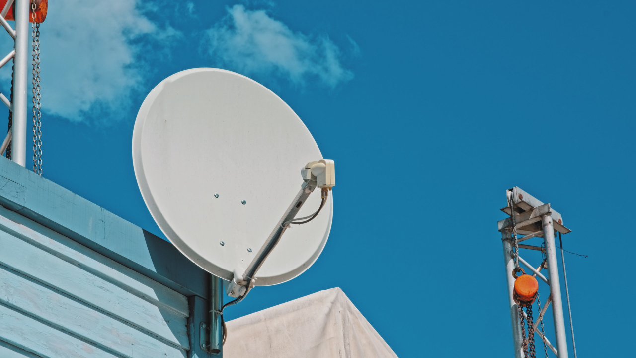 Satellite dish mounted on a blue building against a bright blue sky.