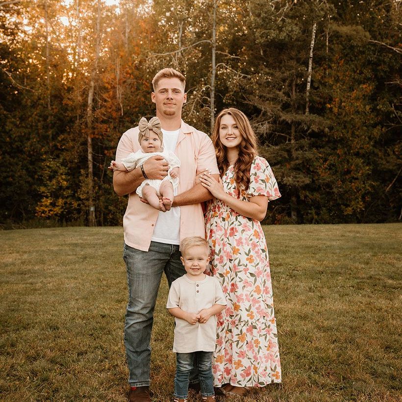 Family of four standing in a field, with two children and autumn trees in the background