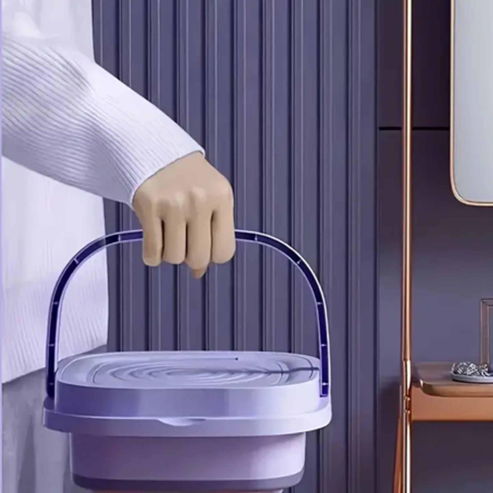 Person holding a light purple, collapsible bucket with a handle. Against a purple-paneled wall.