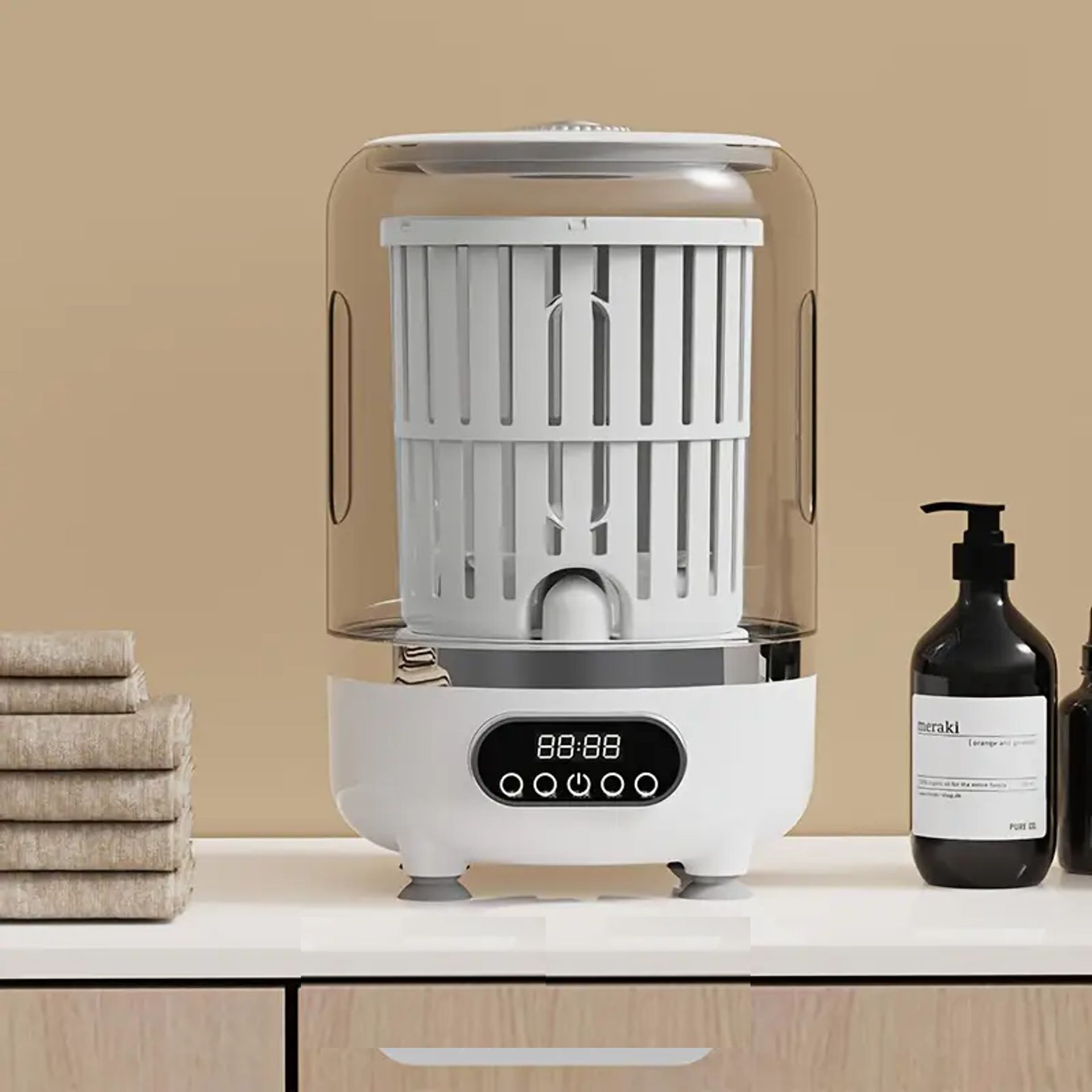 White towel sterilizer on a countertop next to towels and bottles. Clear dome covers the basket.