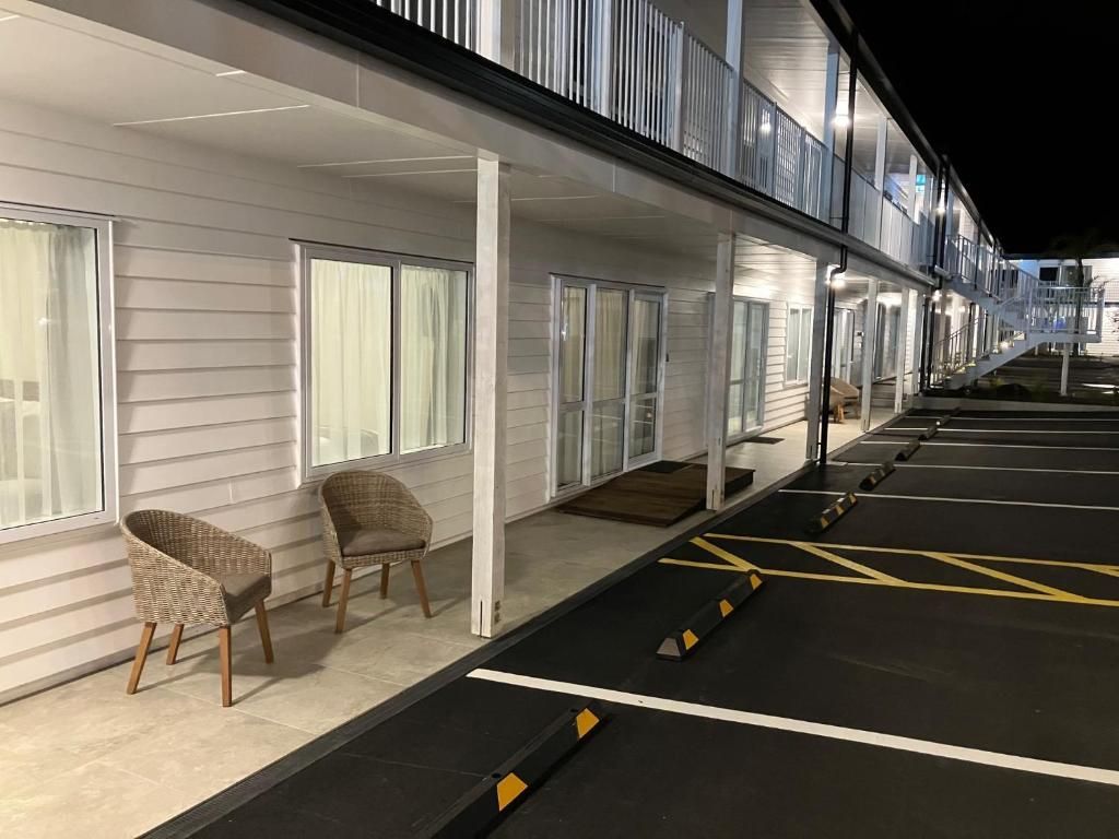 A row of chairs are sitting outside of a building next to a parking lot.