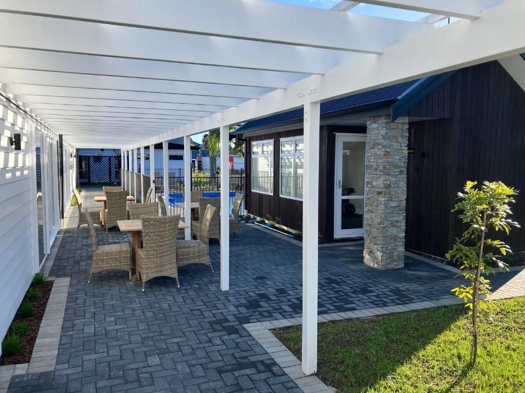 A patio with tables and chairs under a pergola in front of a house.