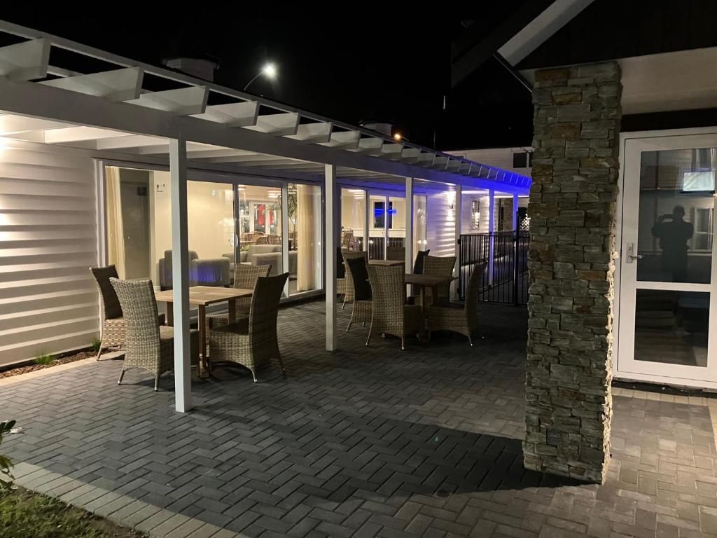 A patio with tables and chairs under a pergola at night.