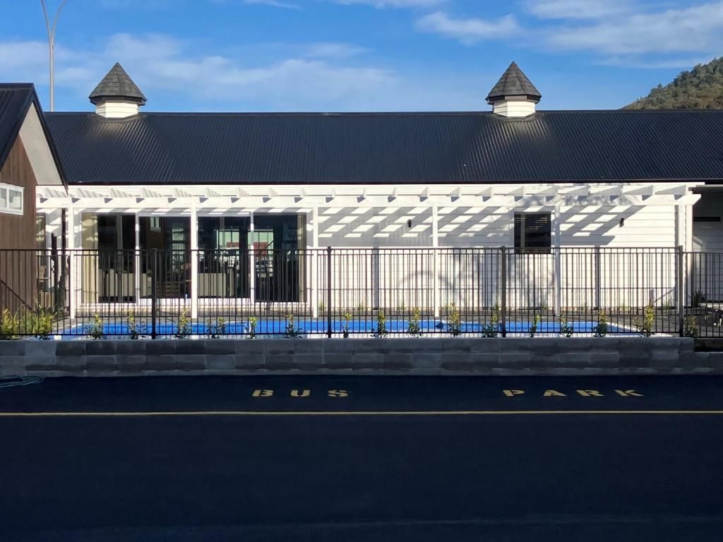 A white house with a black roof and a pool in front of it.