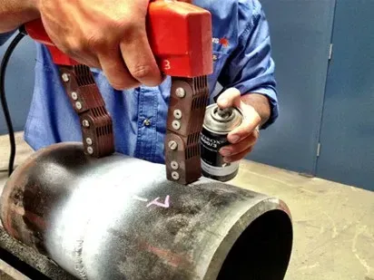 A man is holding a can of spray on a metal pipe to conduct NDT work