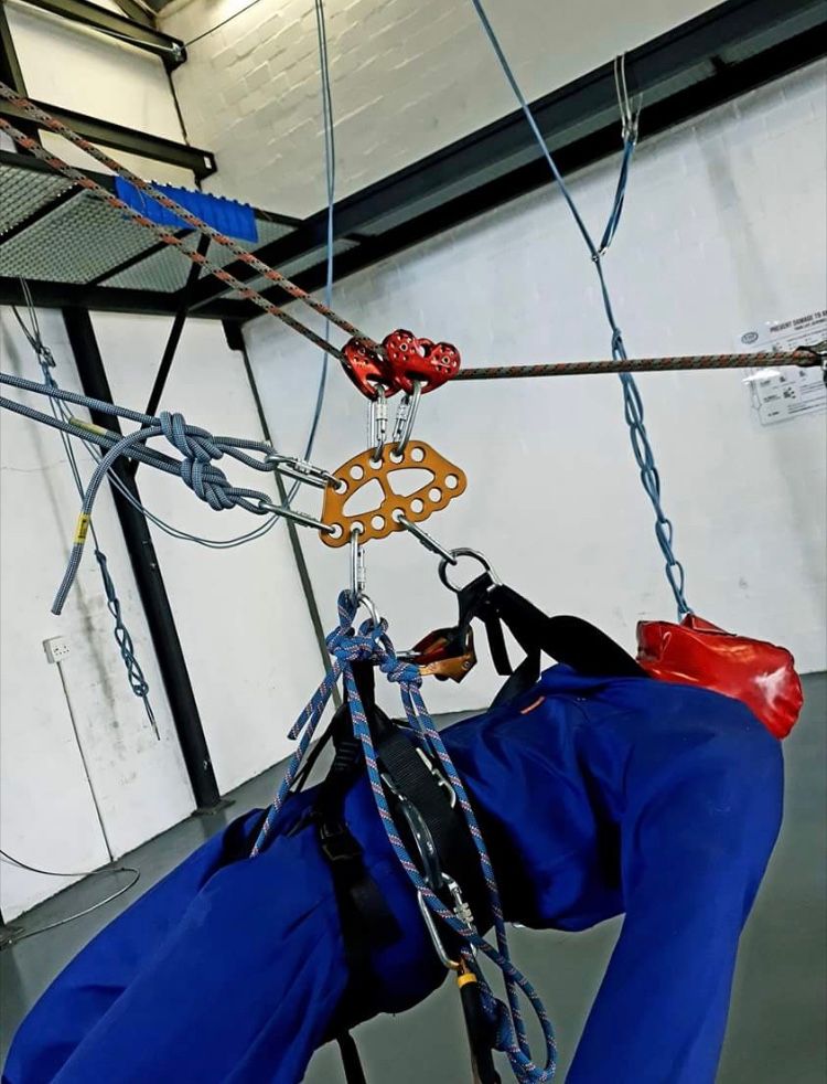 Person in blue jumpsuit harnessed to overhead ropes at an indoor rescue centre.