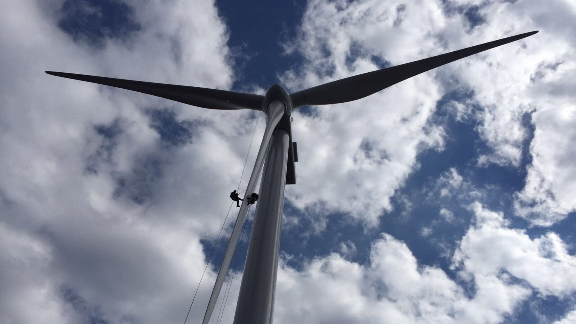 Wind turbine in Northern Ireland against a cloudy blue sky with two abseilers.