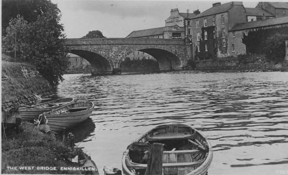 Boats on a river under an arched stone bridge in Enniskillen, with buildings on the right.