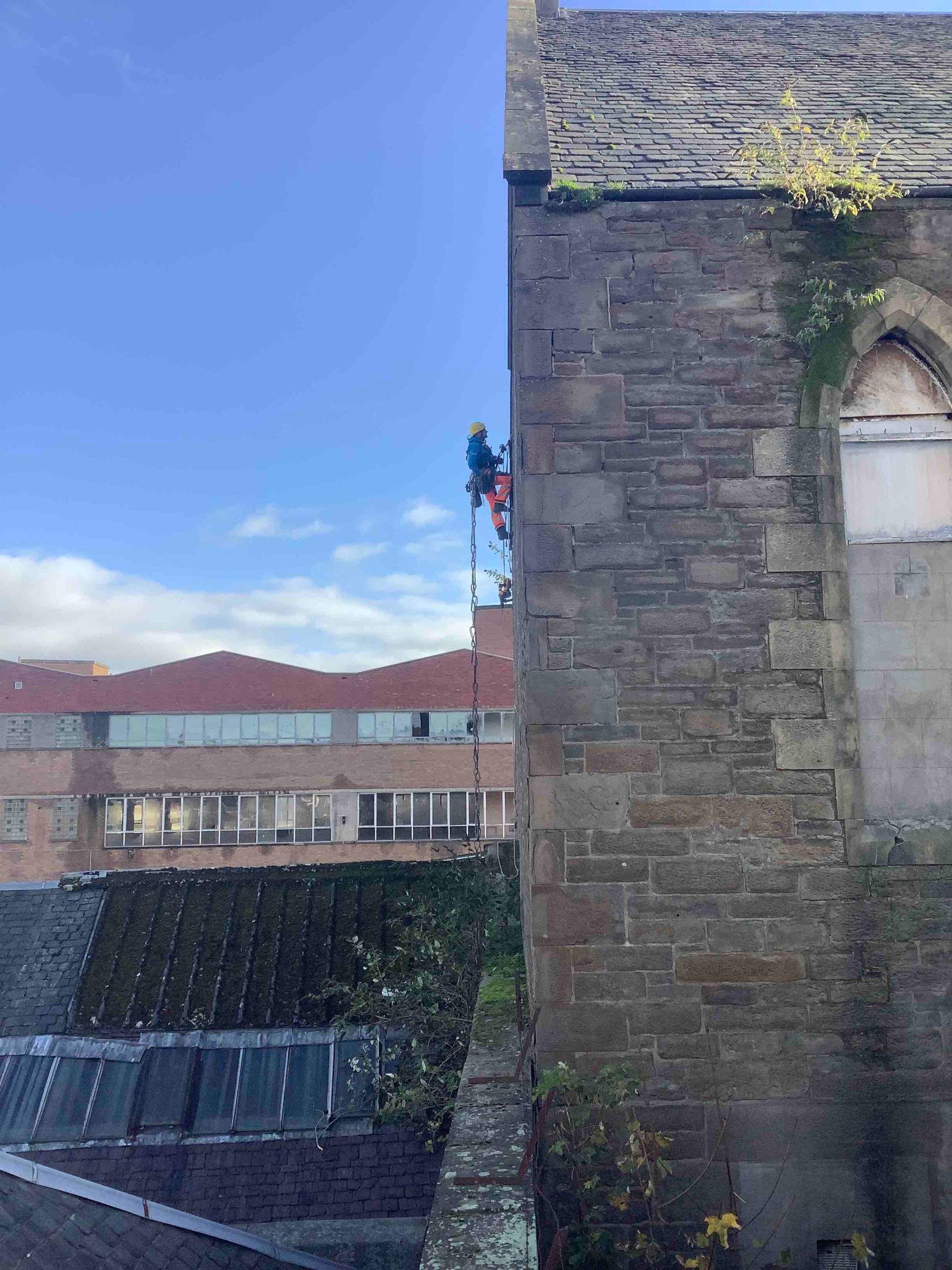 A man is climbing up the side of a brick building as a steeplejack to work.