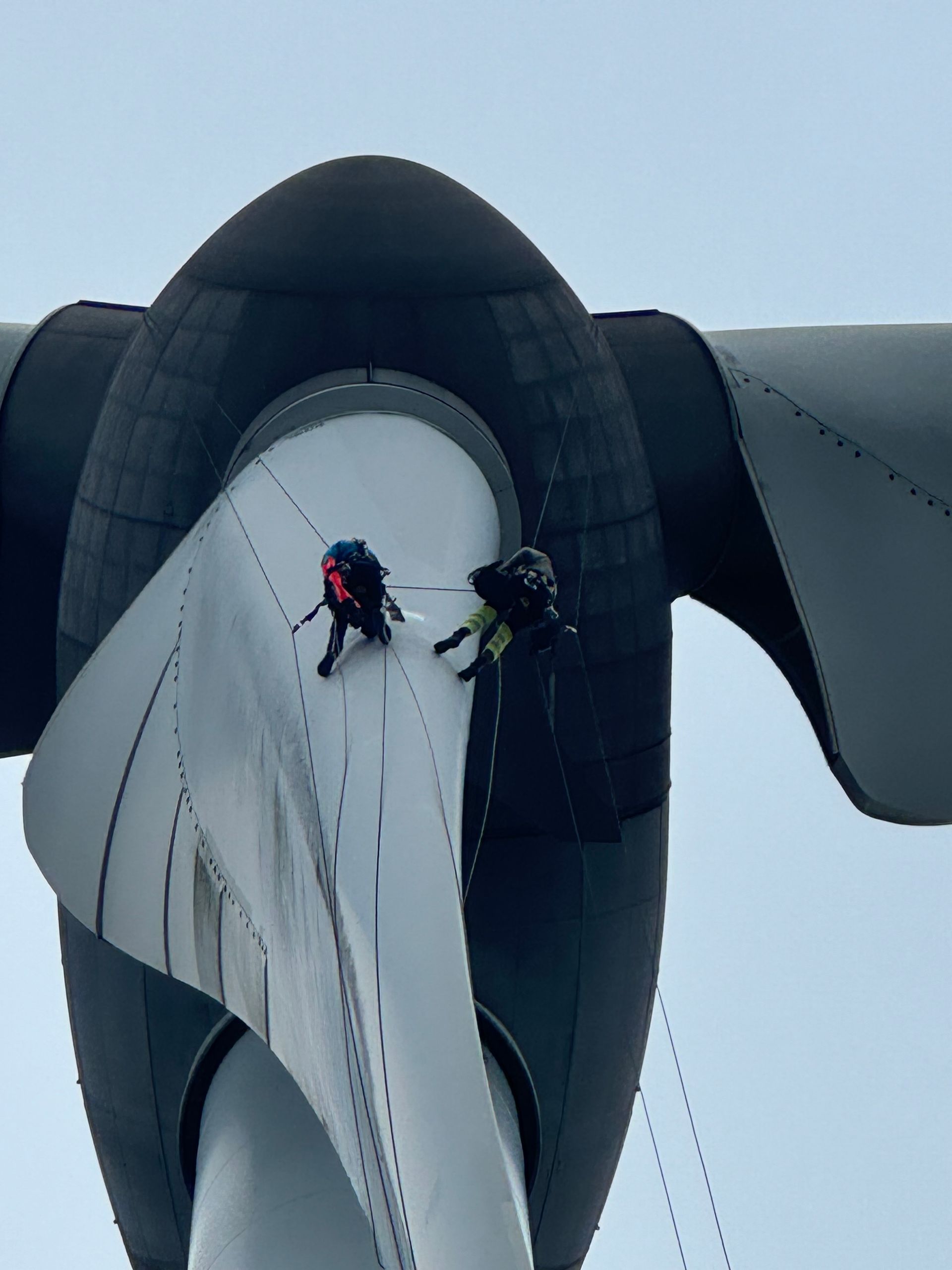 Two men are abseiling down a wind turbine blade