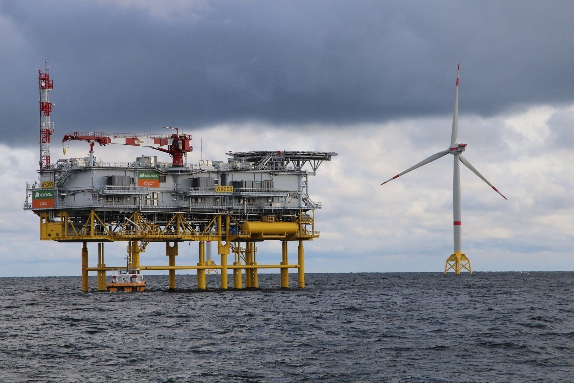 An oil rig in the middle of the ocean with a wind turbine in the background