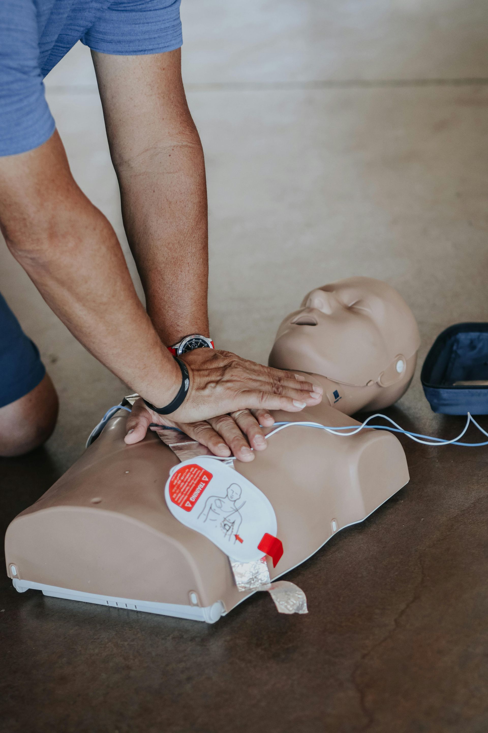 Person performing CPR on a training mannequin with defibrillator pads attached.