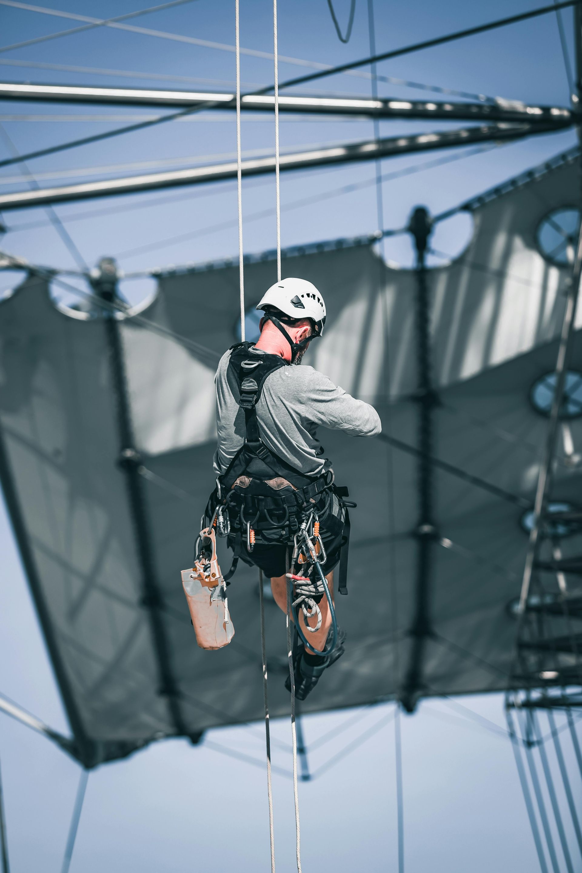 Man in safety harness, inspecting a large, modern structure.