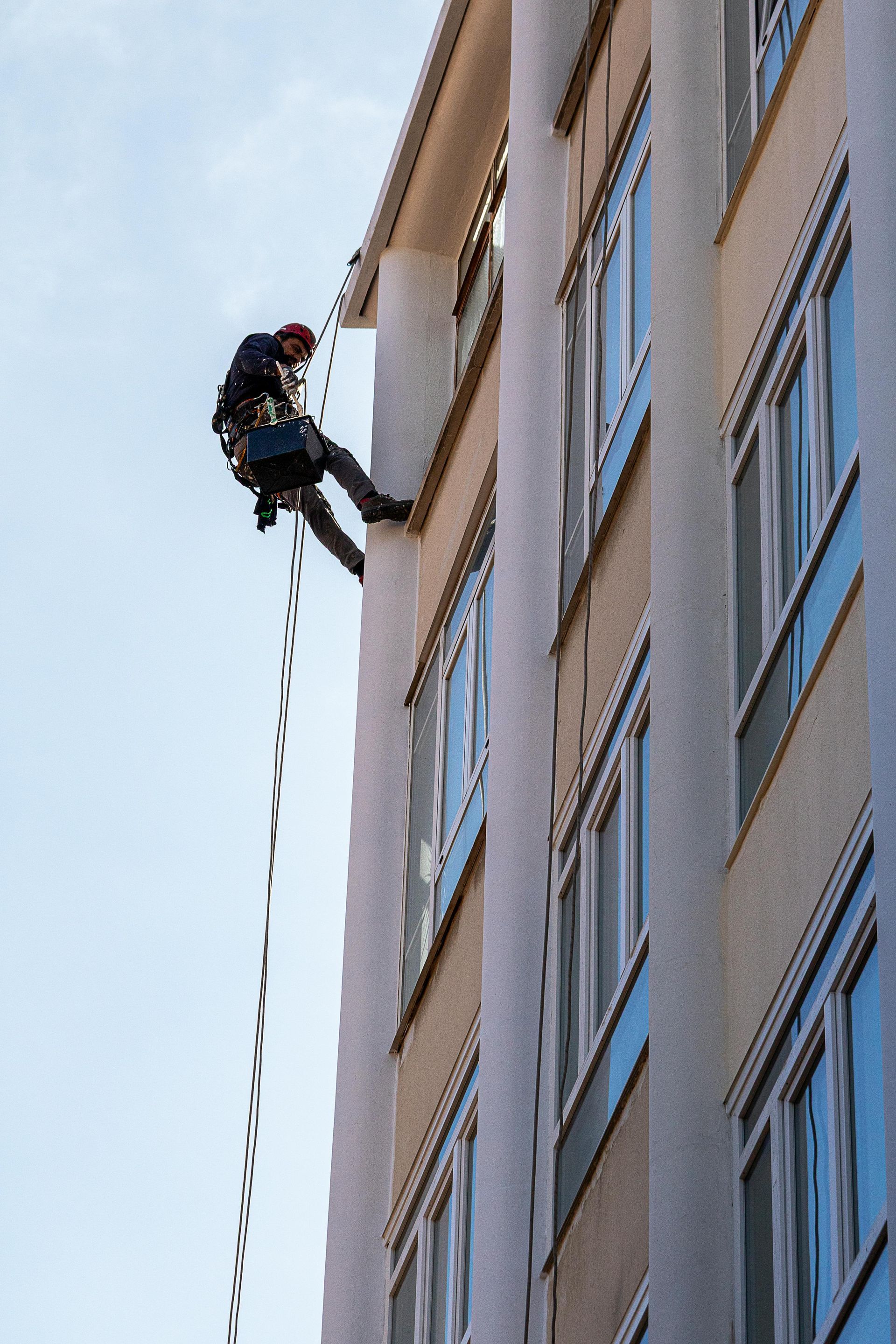 A man is climbing up the side of a tall building on ropes.