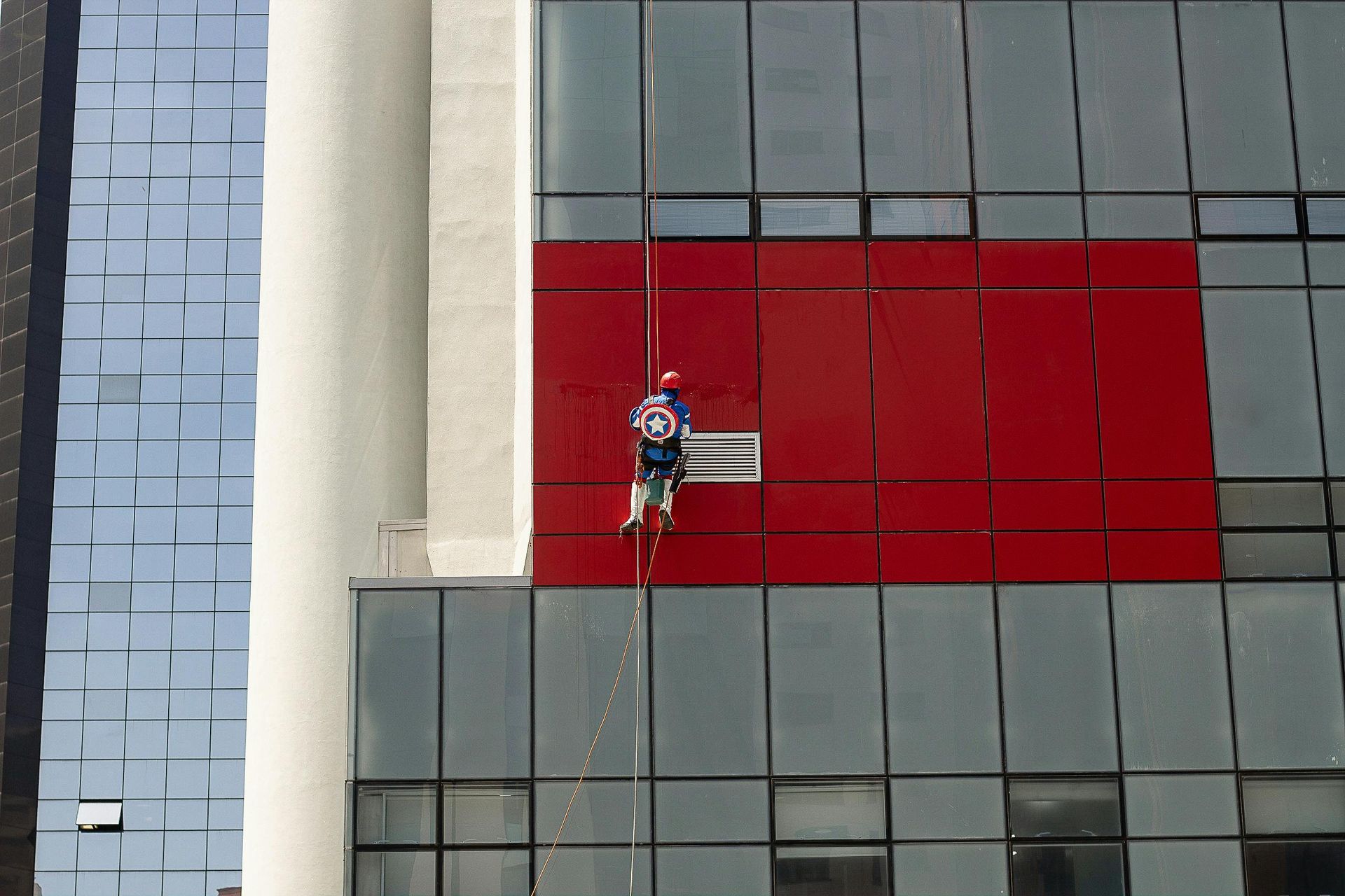 Window washer using rope access to clean a building dressed as captain America. 