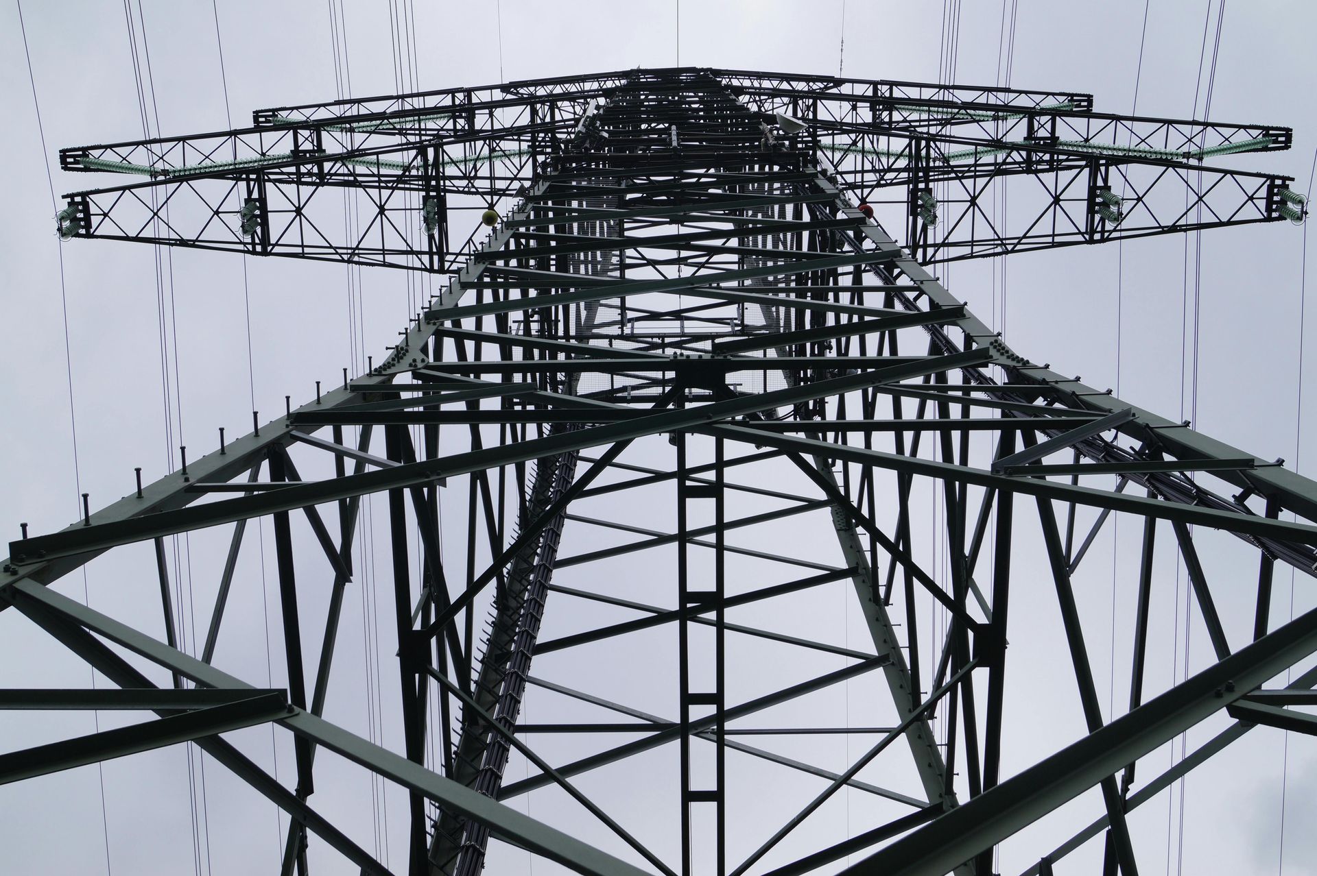 A black and white photo of a very tall overhead line pylon metal structure.