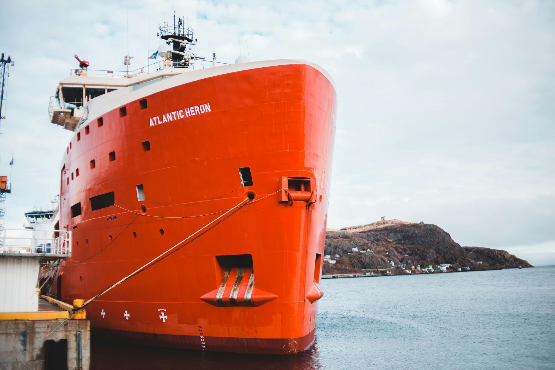 A large red ship receives new marine paint while docked in the water.