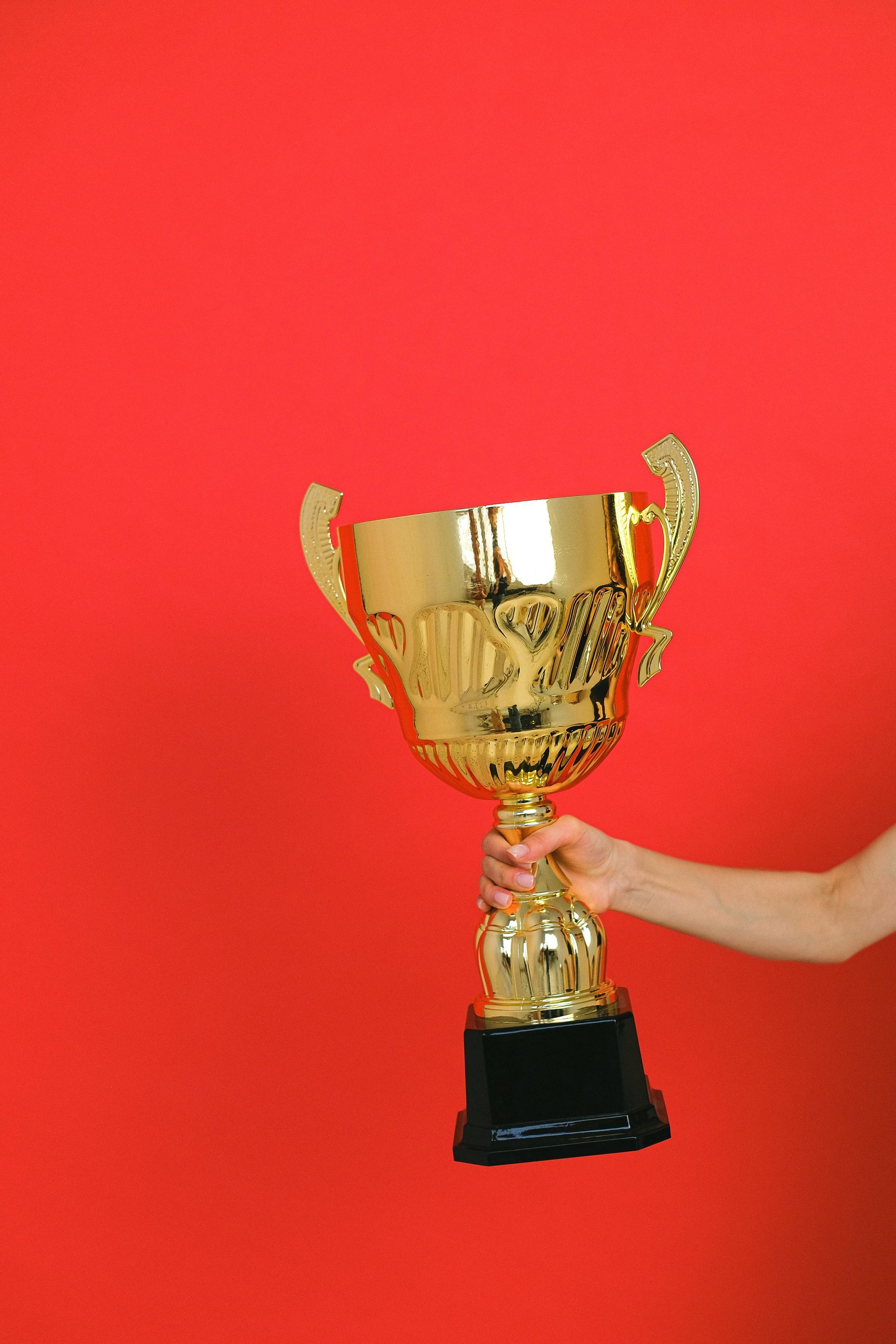 A person's arm holding a large gold trophy against a red background.
