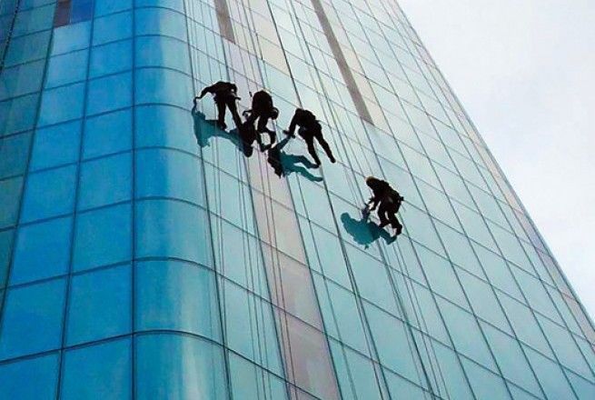 Several climbers rappel down a blue glass skyscraper facade.