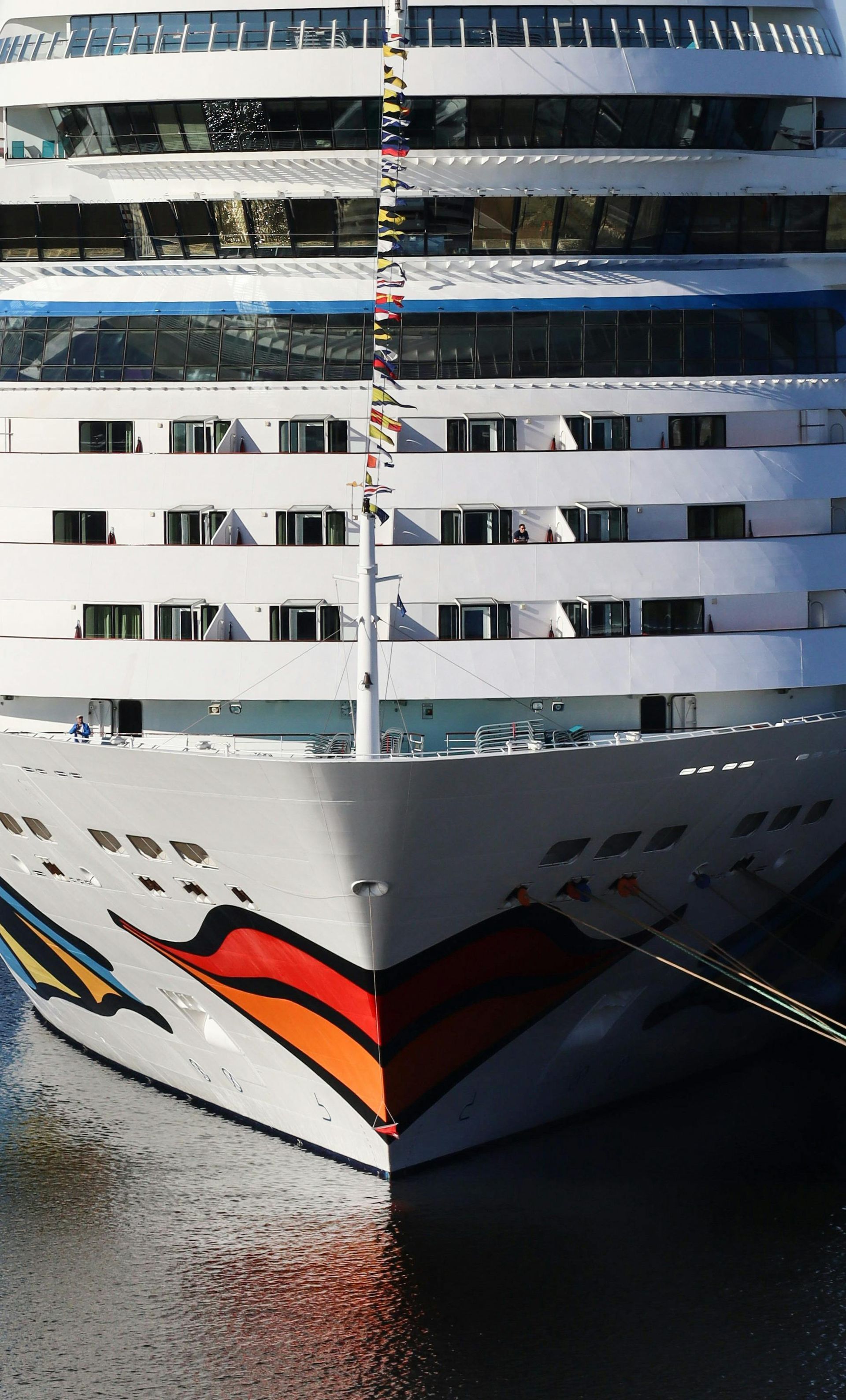 Cruise ship's colourful bow at a dock, with many decks and windows visible.