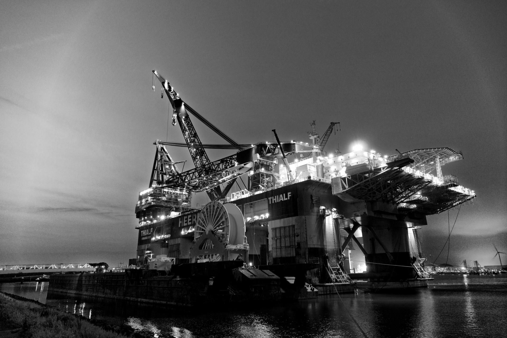 Black and white image of an offshore oil rig at night, illuminated against the dark sky.