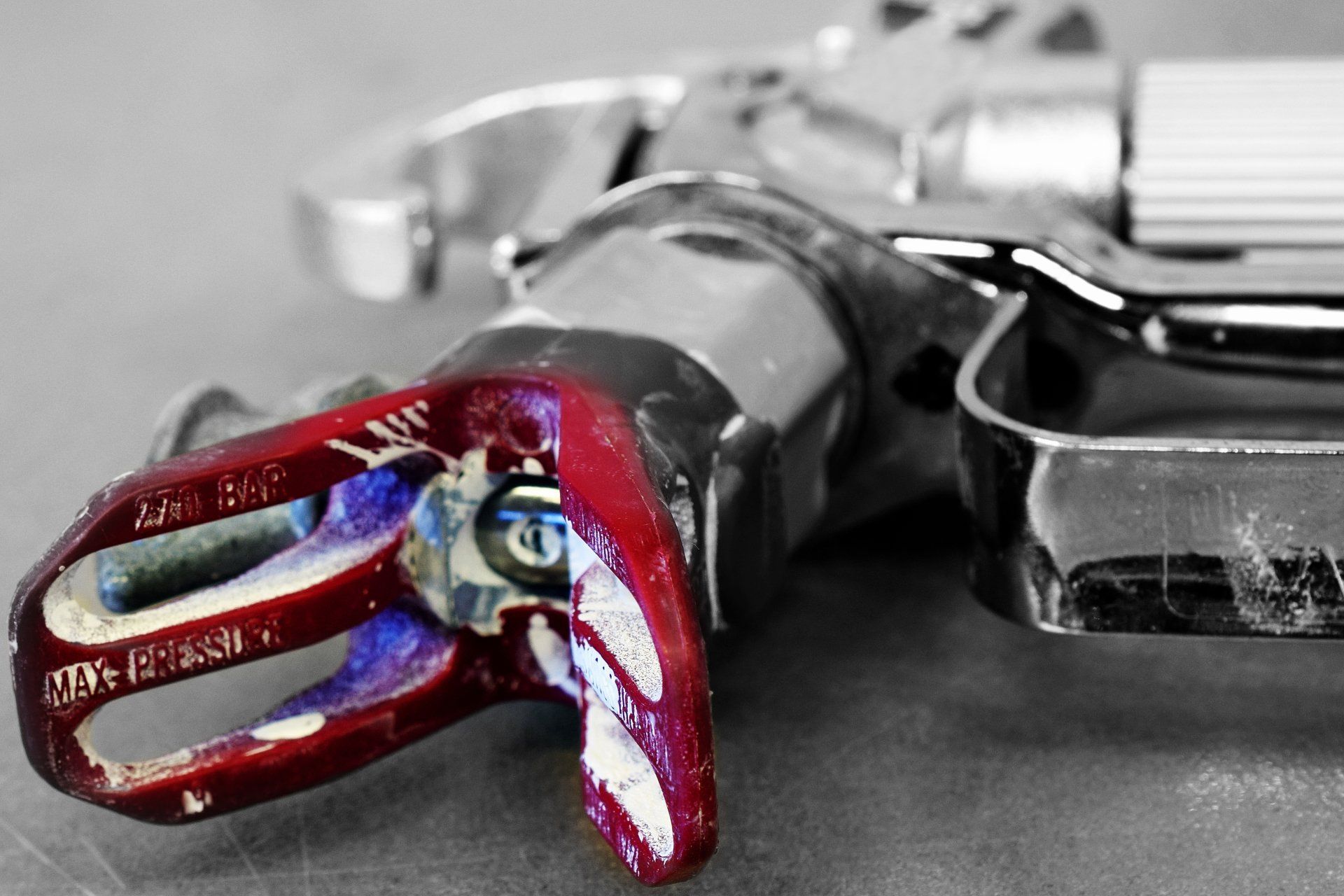 Close-up of a red spray gun trigger with metallic details; the handle and tip is in focus.