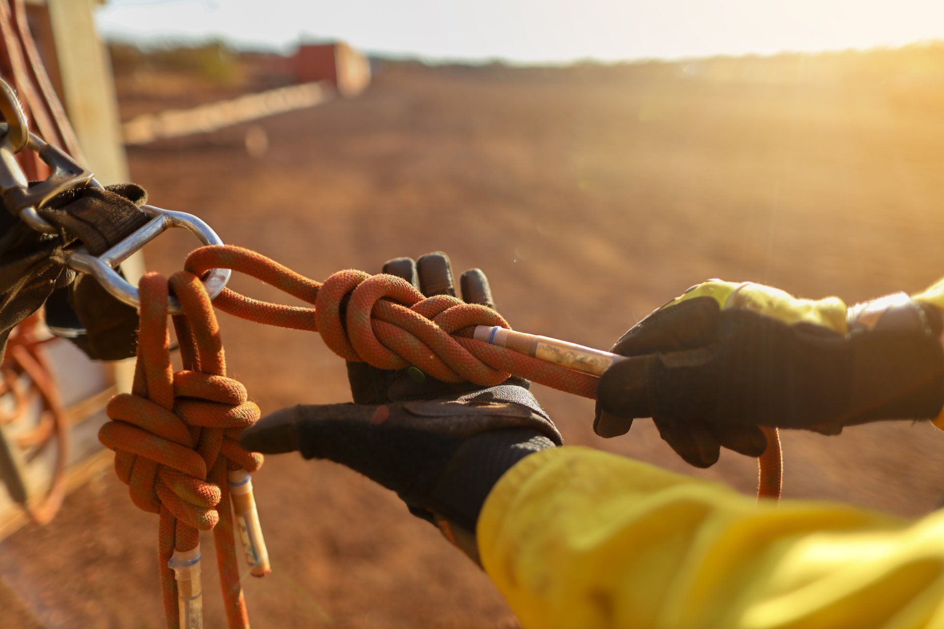 Person in work clothes tying a figure-eight knot on a rope. Outdoor setting with a blurry background.