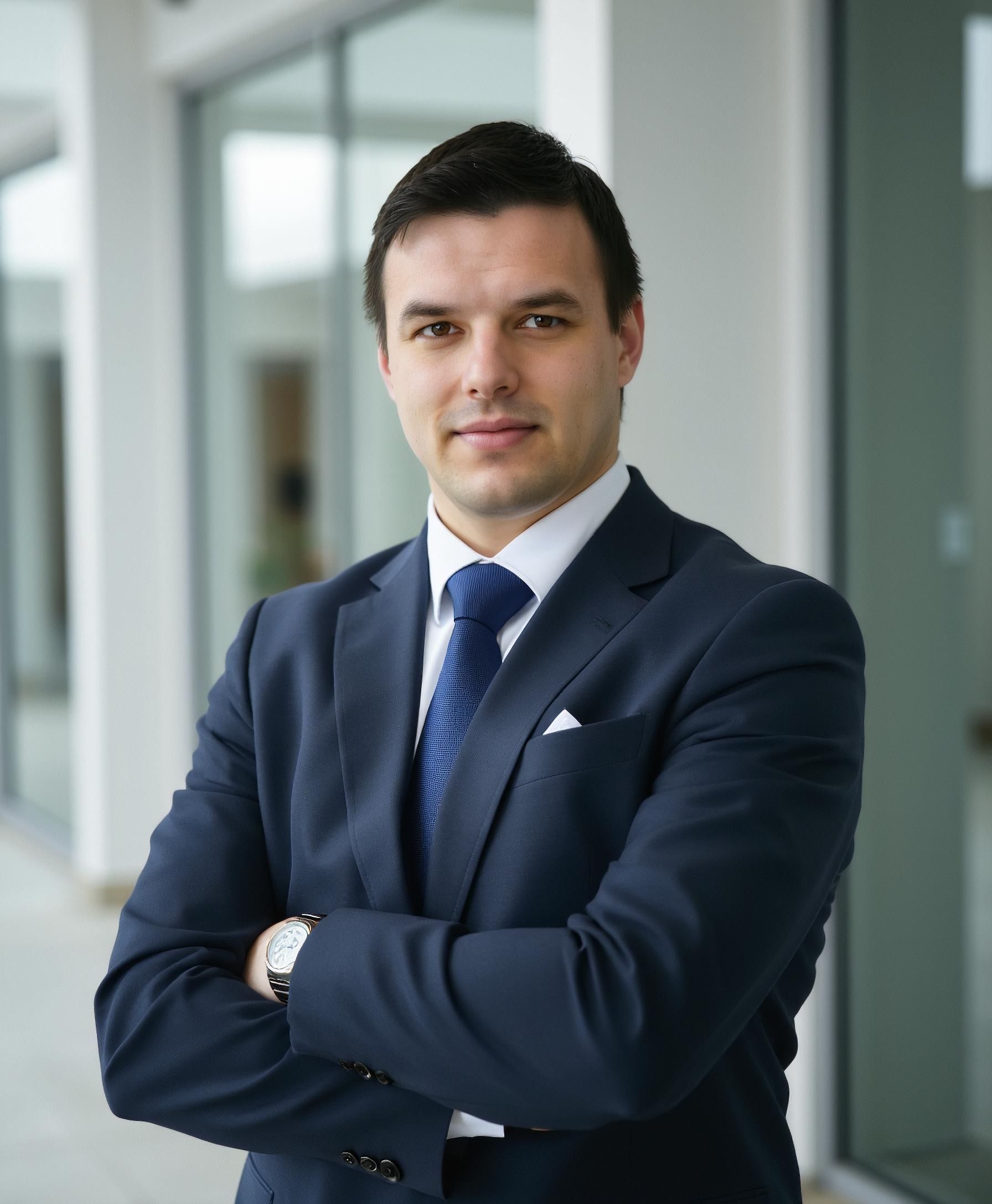 Man in navy suit, arms crossed, smiling. Outdoors, modern building background.