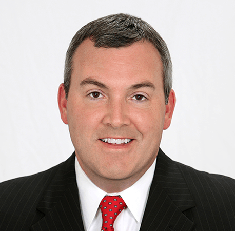 Man in suit and tie smiles, posed against a white backdrop.