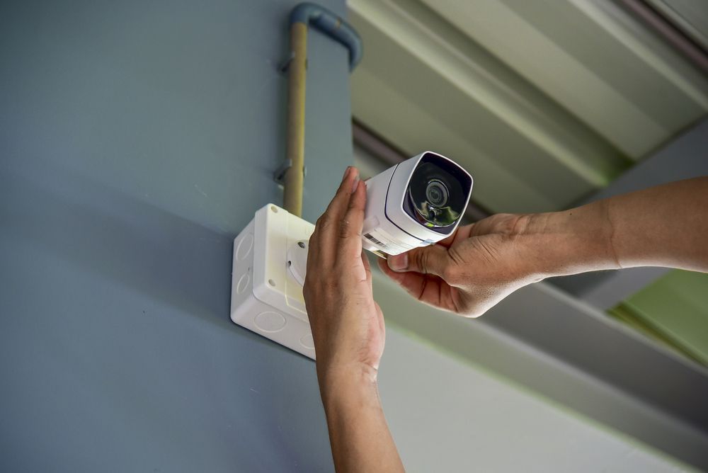 Man Is Installing A Security Camera On A Wall  With Both Hands — Ontime Locksmiths & Security  In Ocean Shores, NSW