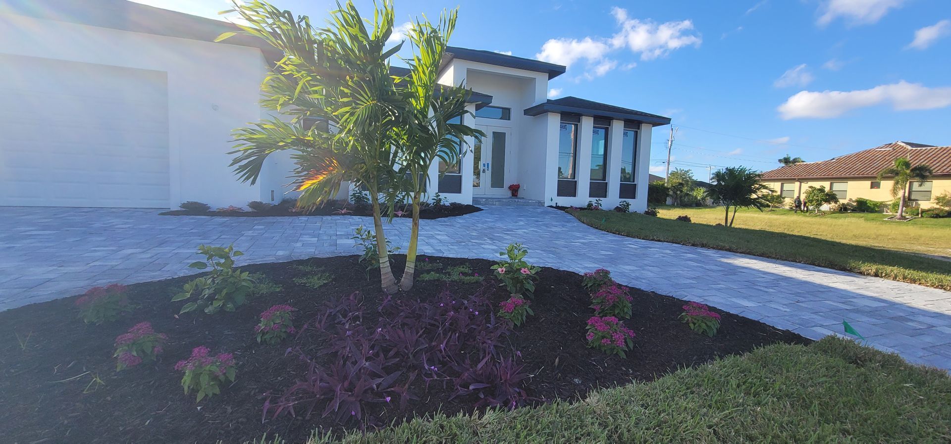 Modern white house with a paved driveway and landscaped yard on a sunny day.