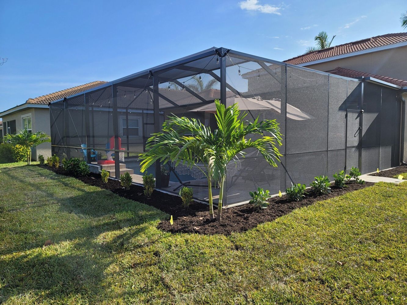 Screened pool enclosure with a black frame and dark mesh, located near a house with landscaping.