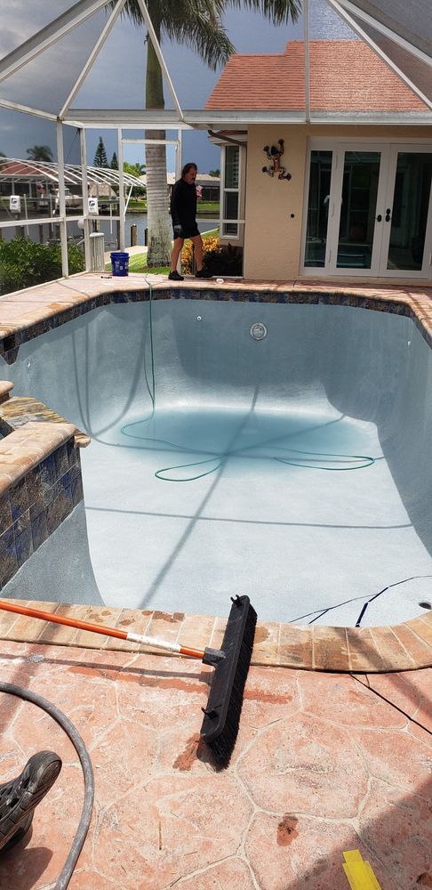 Empty pool with person near a house. Pool equipment is on the deck, enclosed by a screen.